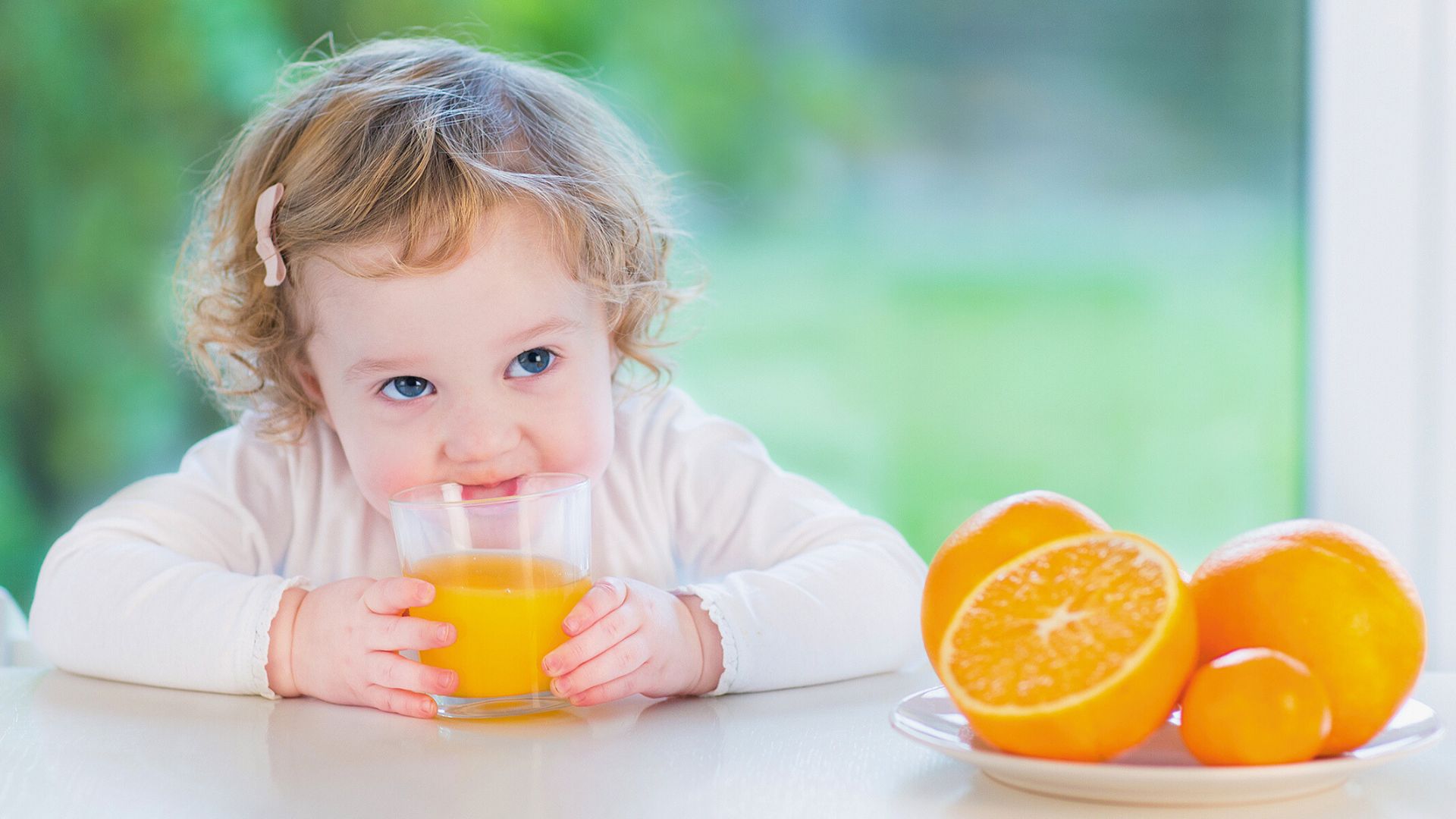 Toddler holding a glass of orange juice at a table