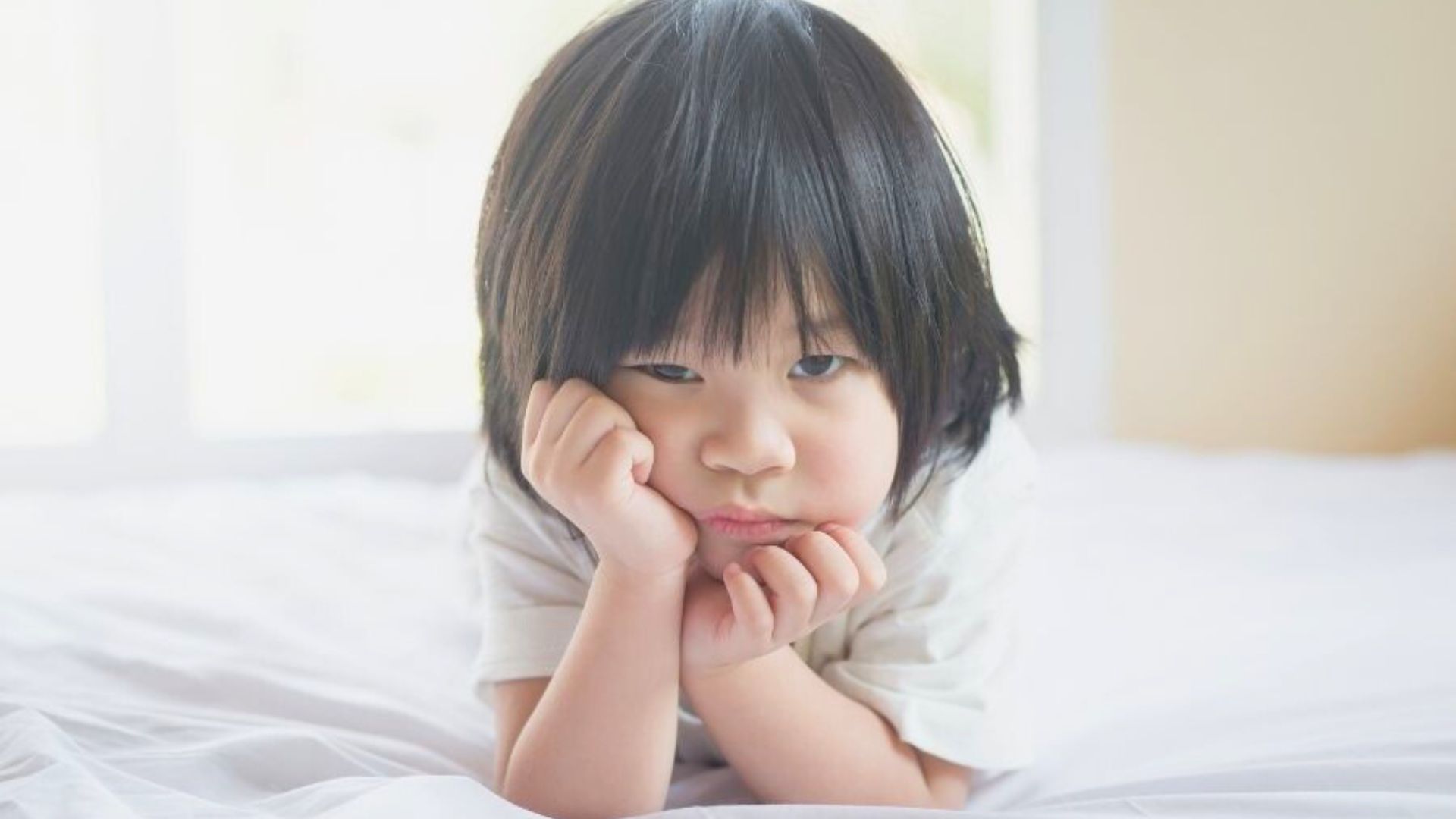 oddler lying on a bed with chin resting on hands, looking bored or uninterested during an activity