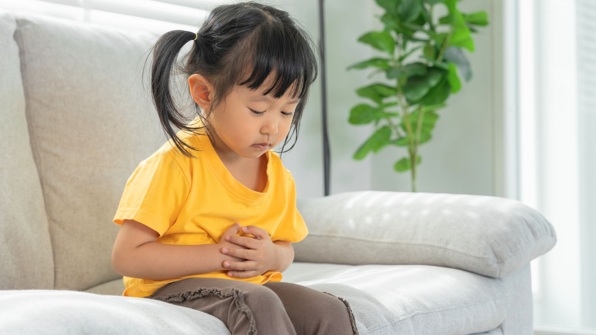 Toddler sitting on a couch holding their stomach, experiencing constipation and digestive discomfort