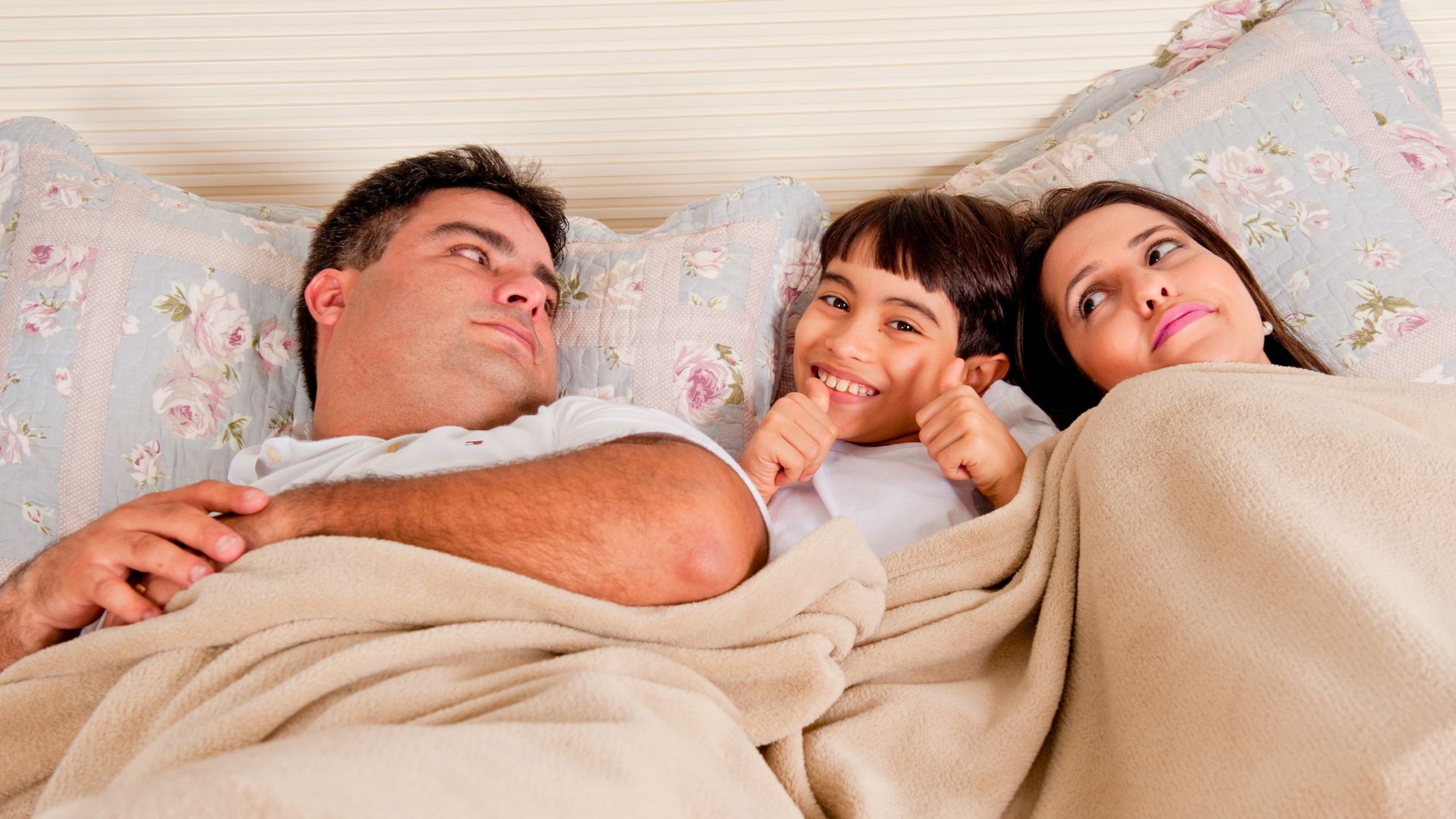 Parents lying in bed with their child between them, illustrating intimacy challenges and family dynamics after having children