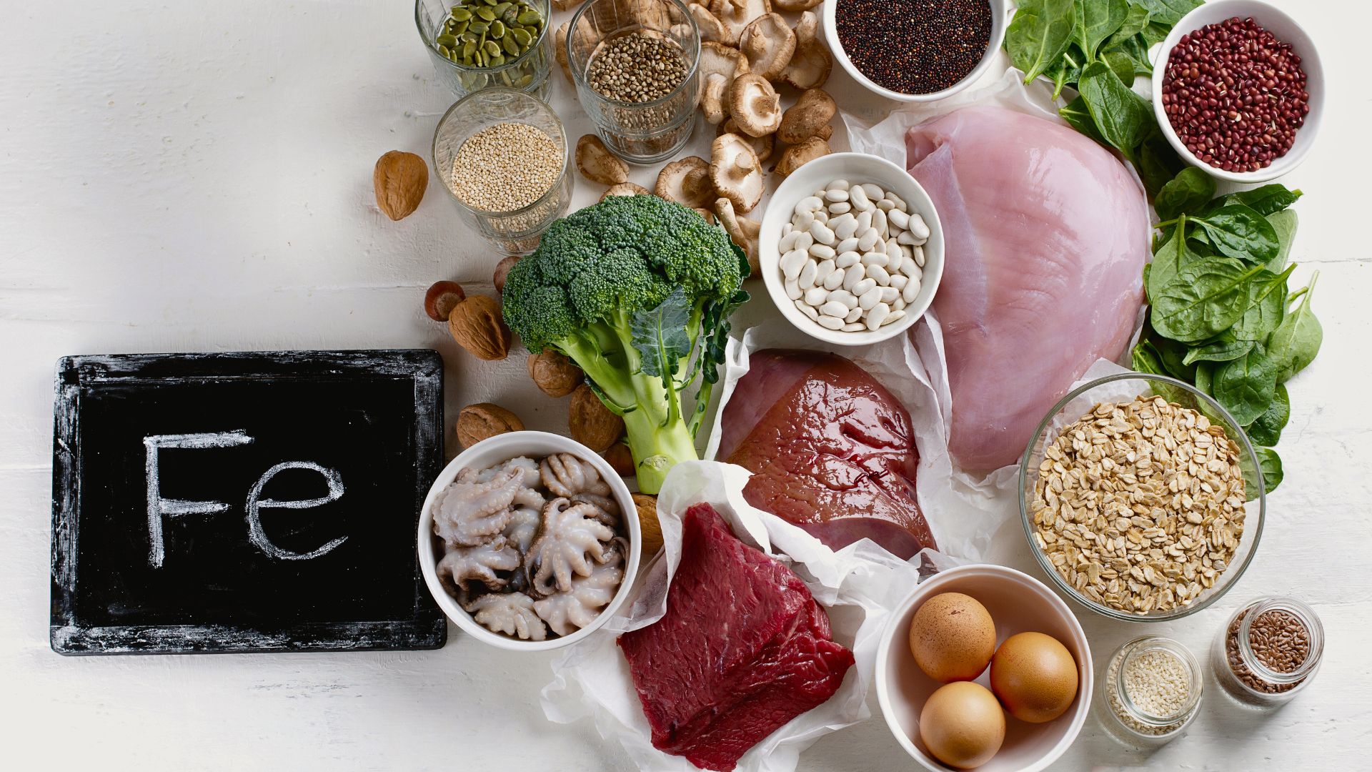 Selection of iron rich foods including meat, eggs, legumes, grains, and vegetables arranged on a table