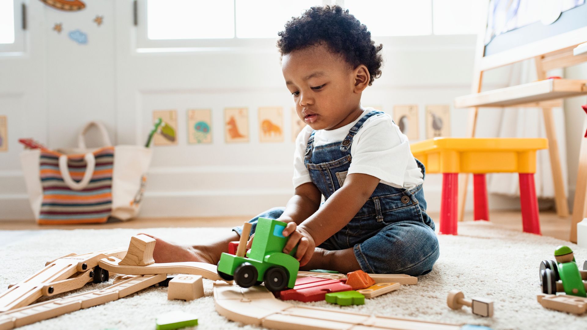 Keep Toddler Busy and Interested Toddler sitting on the floor playing with wooden train tracks and toy vehicles, focused and engaged in independent play