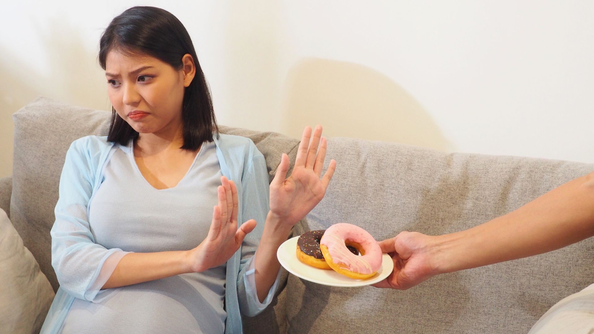 Pregnant woman sitting on a couch declining a plate of food, illustrating loss of appetite during pregnancy