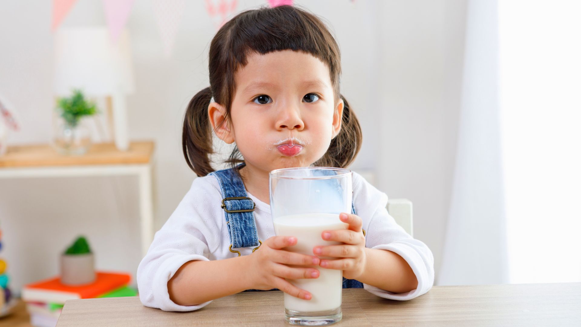 Toddler sitting at a table drinking whole milk from a glass