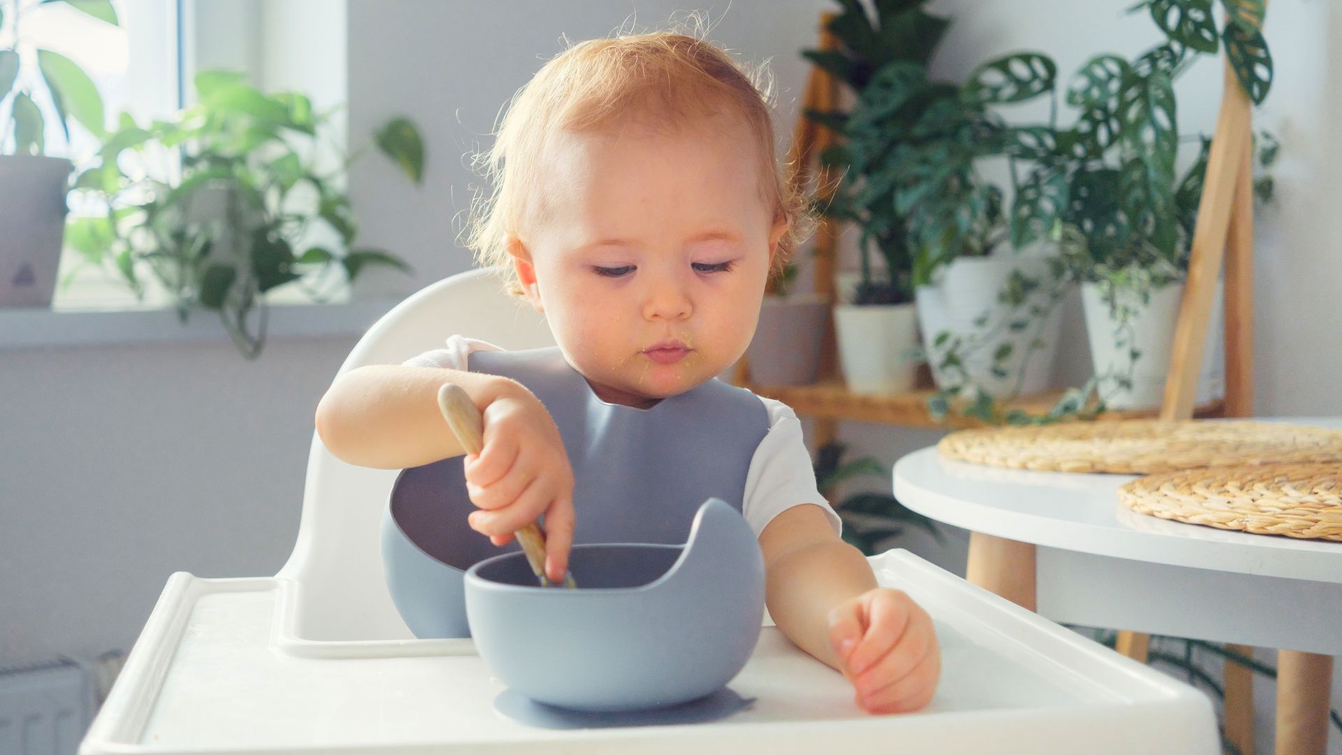 Baby sitting in a high chair using a spoon to eat independently